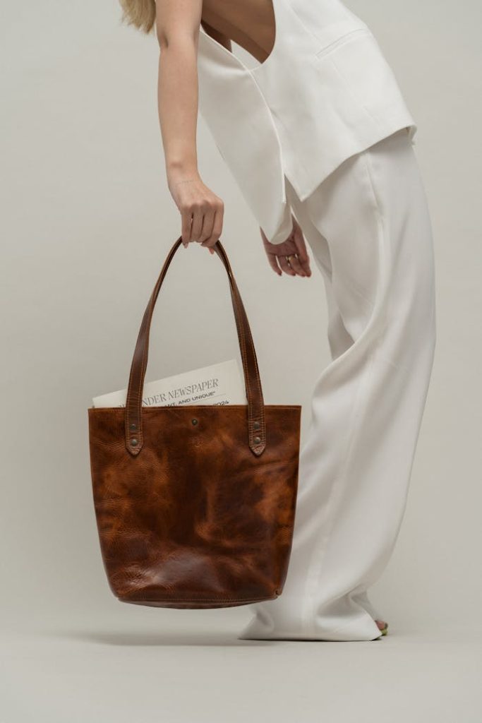 Stylish woman holding a brown leather bag in a minimalist studio setting.